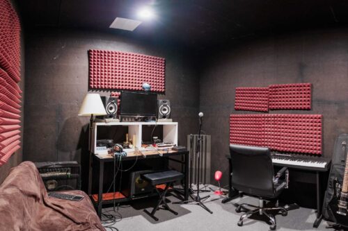 A music recording studio at Sonance Rehearsal Studios Brown Lane location with soundproof foam on the walls, a desk with computer and audio equipment, a chair, a sofa, and a keyboard.