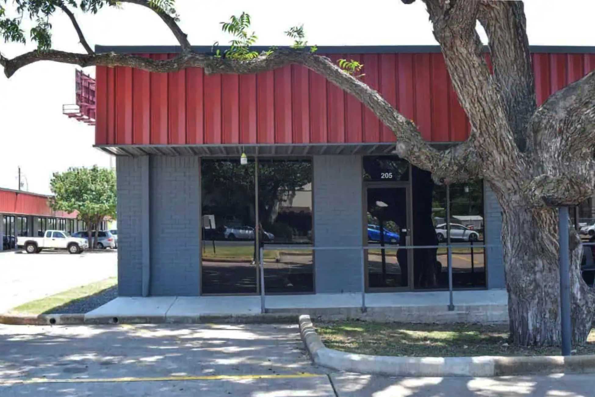 The Sonance Rehearsal Studios Ed Bluestein location, a gray and red commercial building of rehearsal rooms with large windows and a tree in front.